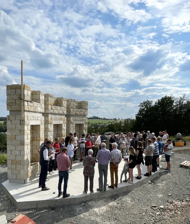 Construction: partial wall built with two columns, people gathered around, clear sky