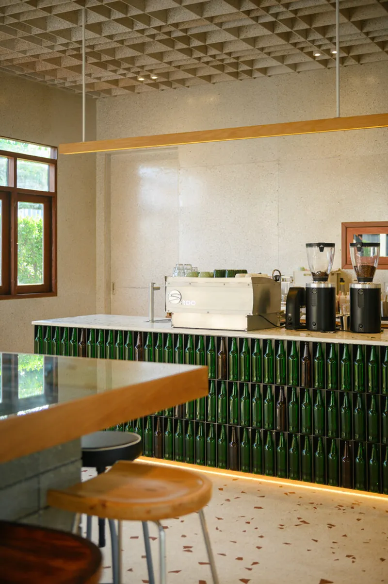 Counter detail: green glass bottles set vertically as bar front, terrazzo top, timber bar ledge