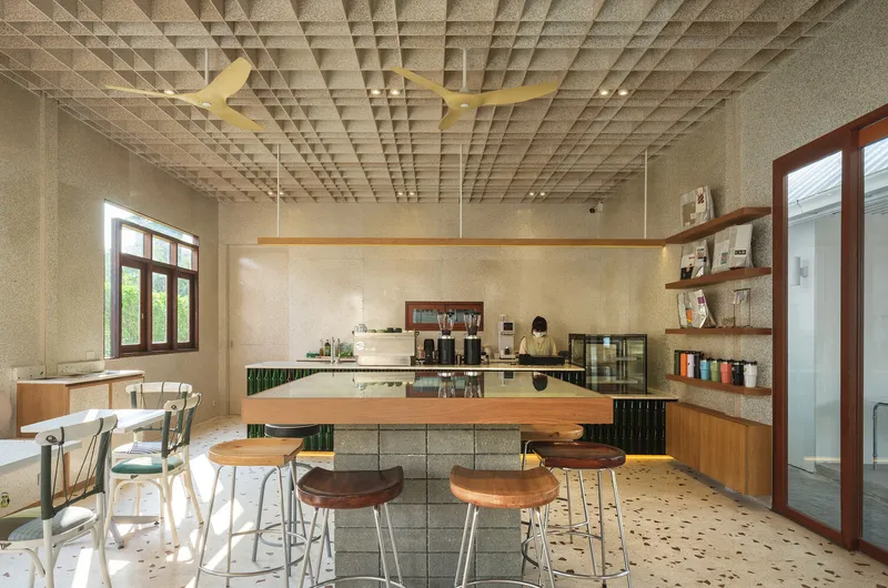 Full interior: waffle ceiling with fans, bar stools at counter, tables along window wall, terrazzo floor