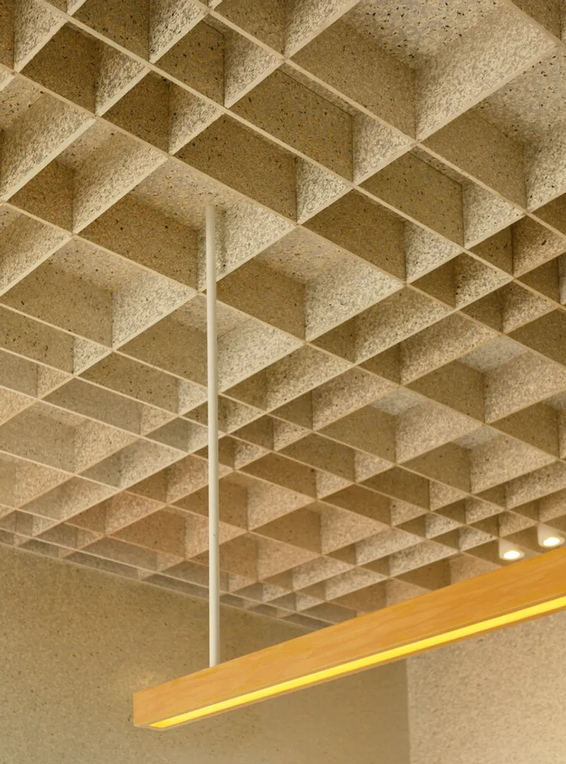 Ceiling detail: exposed waffle grid in recycled material with timber light bar and brass fan