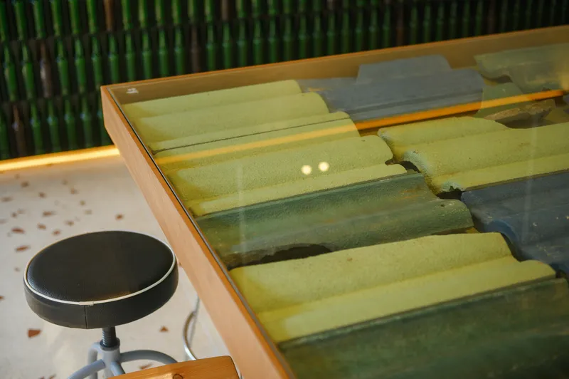 Counter table detail: reclaimed roof tiles under glass top, bar stool beside green bottles