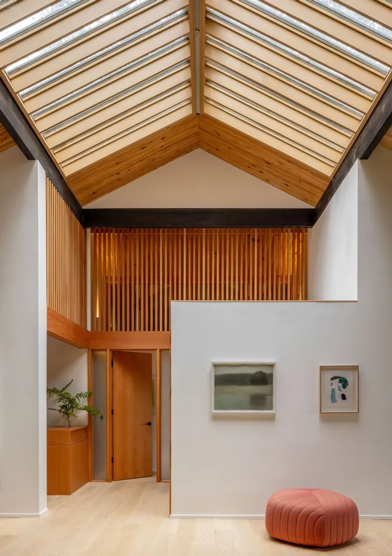 Double-height interior space with timber-slatted mezzanine and striped skylight overhead