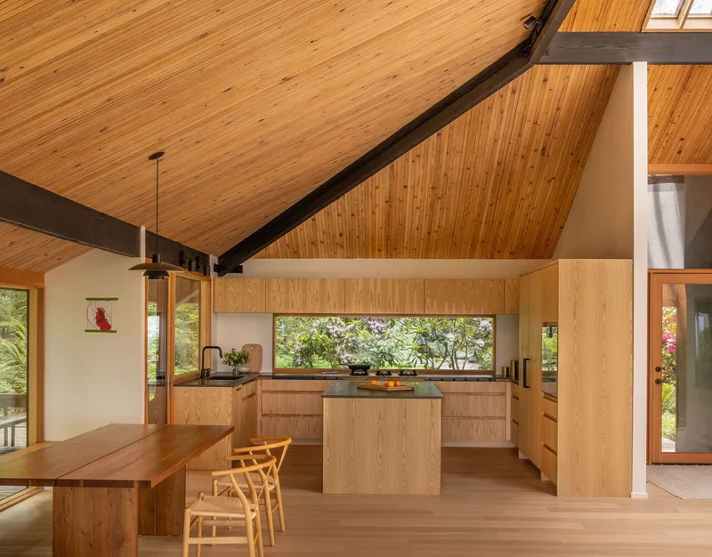 Open kitchen with oak cabinetry and horizontal window strip beneath a vaulted wood ceiling