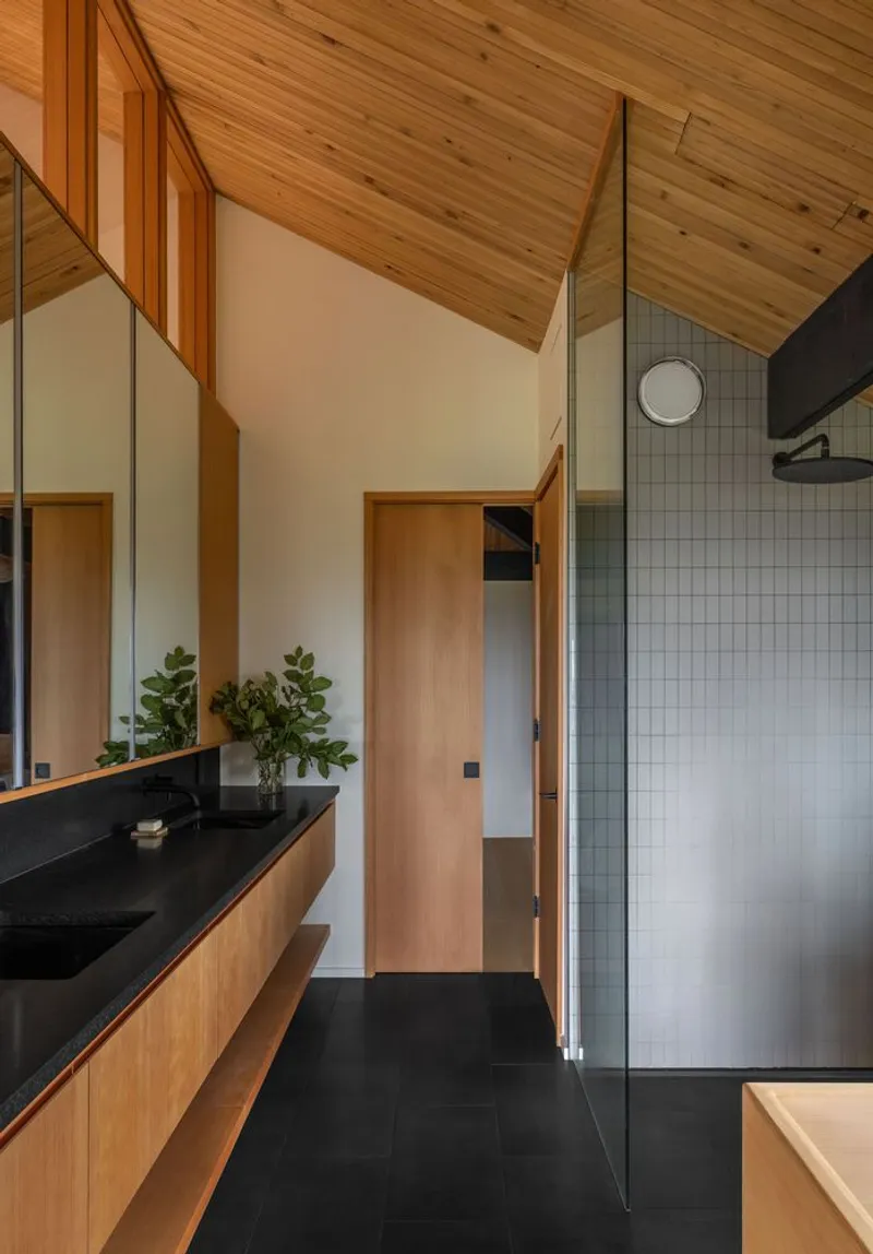 Bathroom interior with timber vanity, black stone countertop, and angled timber ceiling above small tile shower enclosure
