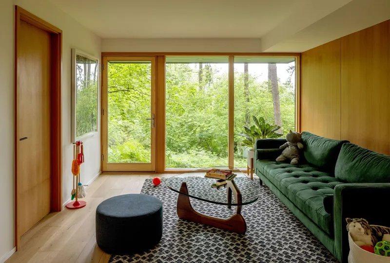 Living area with floor-to-ceiling glass doors opening to undergrowth and timber columns beyond