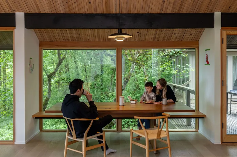 Dining nook with three people seated at timber table beneath slatted wood ceiling and pendant light