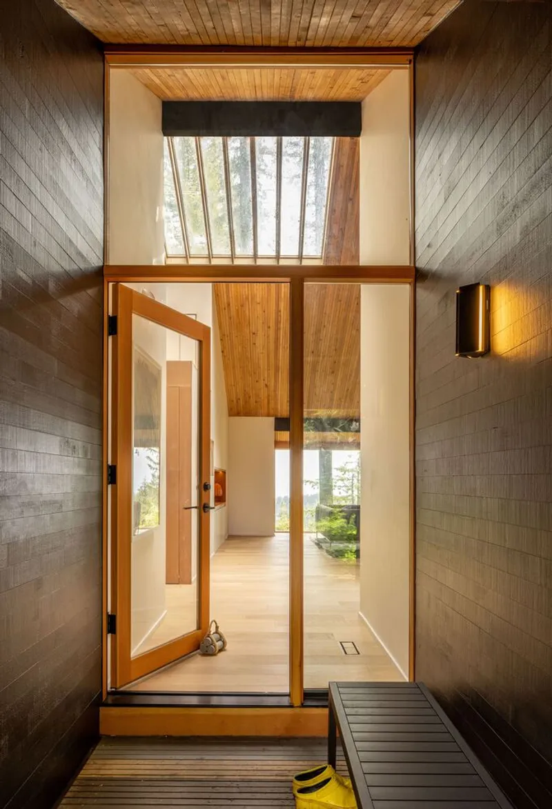 Entry vestibule with timber door opening to a double-height glazed wall and slatted wooden ceiling