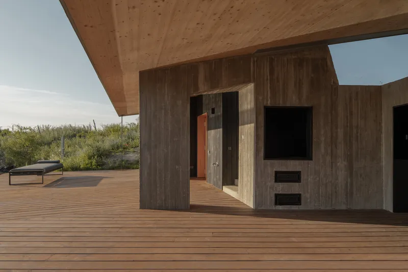 Deck detail: charred timber and concrete wall with built-in fireplace and TV recess, timber deck, meadow beyond