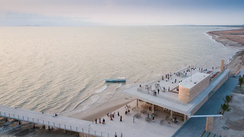Rooftop terrace and beach plaza filled with visitors at dusk beside still coastal waters