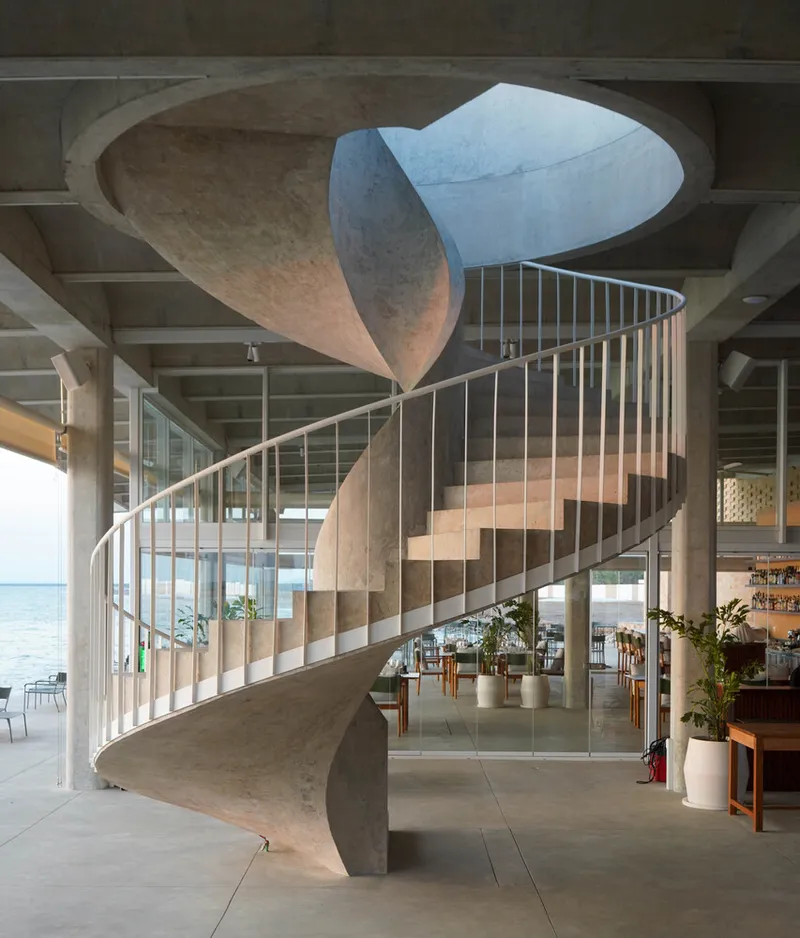 Sculptural concrete spiral staircase with metal balustrade rising through an oval ceiling opening