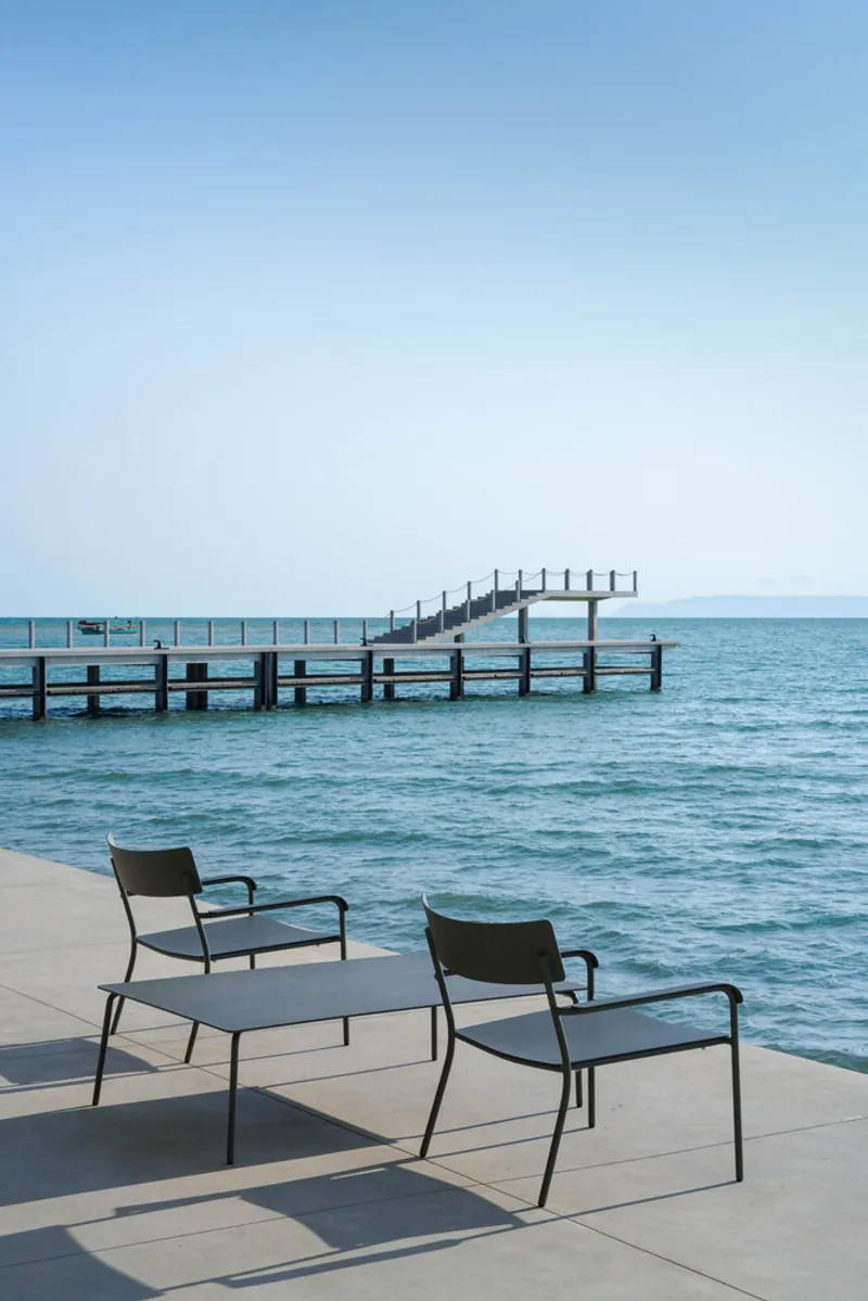 Two lounge chairs on the waterfront terrace overlooking a timber pier extending into the sea
