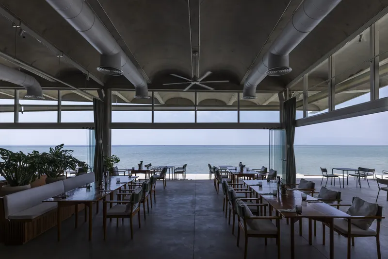 Interior dining space with exposed ductwork ceiling and full-height glazing framing ocean views