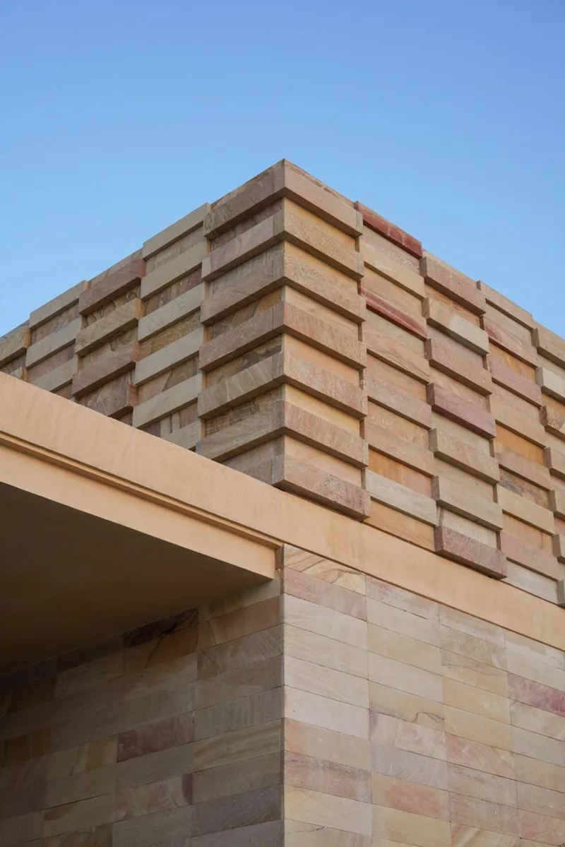 Corner detail of layered sandstone block facade against a clear blue sky