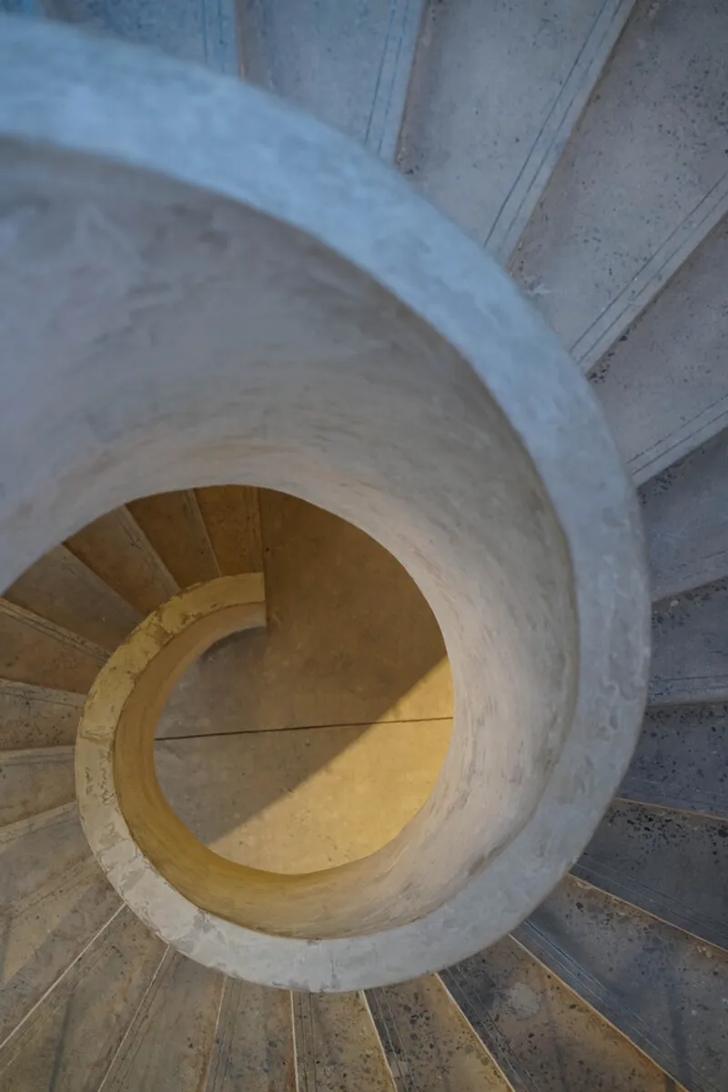 Top-down view of spiral concrete staircase with warm light illuminating the curved center void
