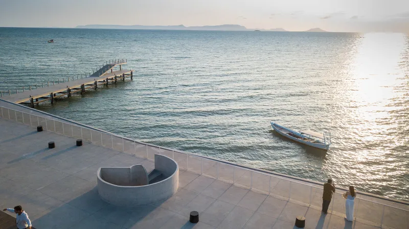 Curved concrete seating element on the terrace plaza with visitors at sunset near the water's edge