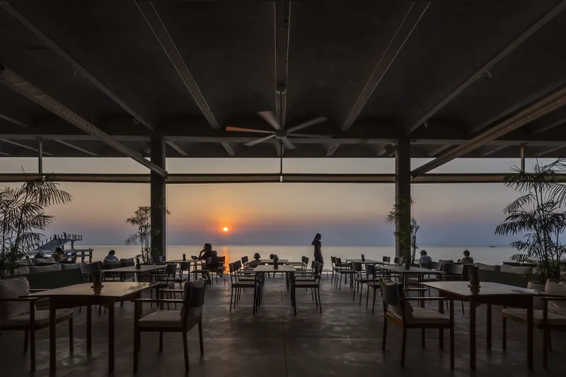 Restaurant interior with exposed steel beams and ceiling fan framing sunset views over the water