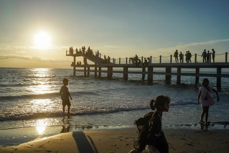 Timber pier extending into the ocean with visitors silhouetted against the setting sun