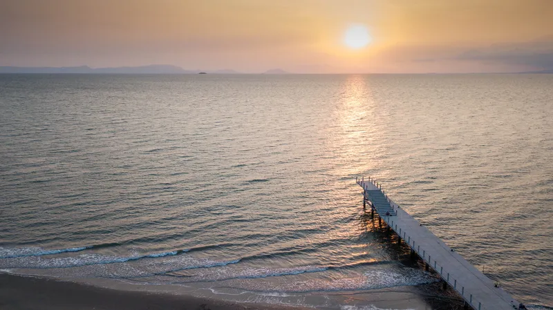 Aerial view of white concrete jetty stretching into calm water at golden hour