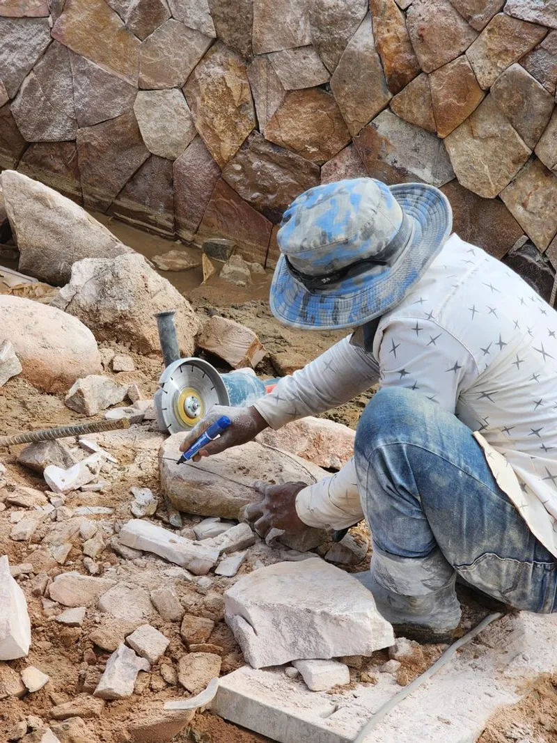 Worker cutting stone blocks with a handheld angle grinder against a rubble stone wall