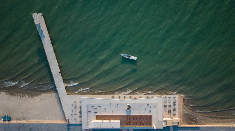 Aerial view of a concrete pier extending into green coastal water with a small boat nearby