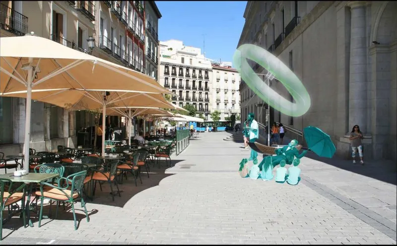 Daytime street deployment: the Ringsail with its inflatable ring and cyan performers beside cafe terraces and parasols on a sunny Madrid pavement near Plaza de Oriente
