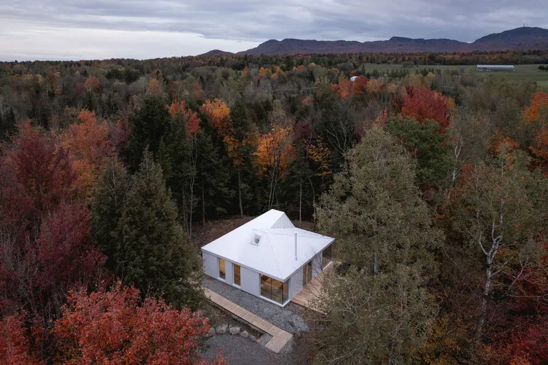 Aerial: white metal roof among red and orange autumn canopy, Eastern Townships mountains in the distance