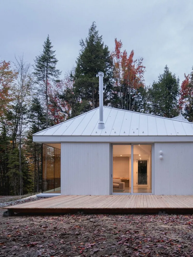 Corner view: white metal cladding, cedar deck, twin roof slopes with skylights, autumn trees