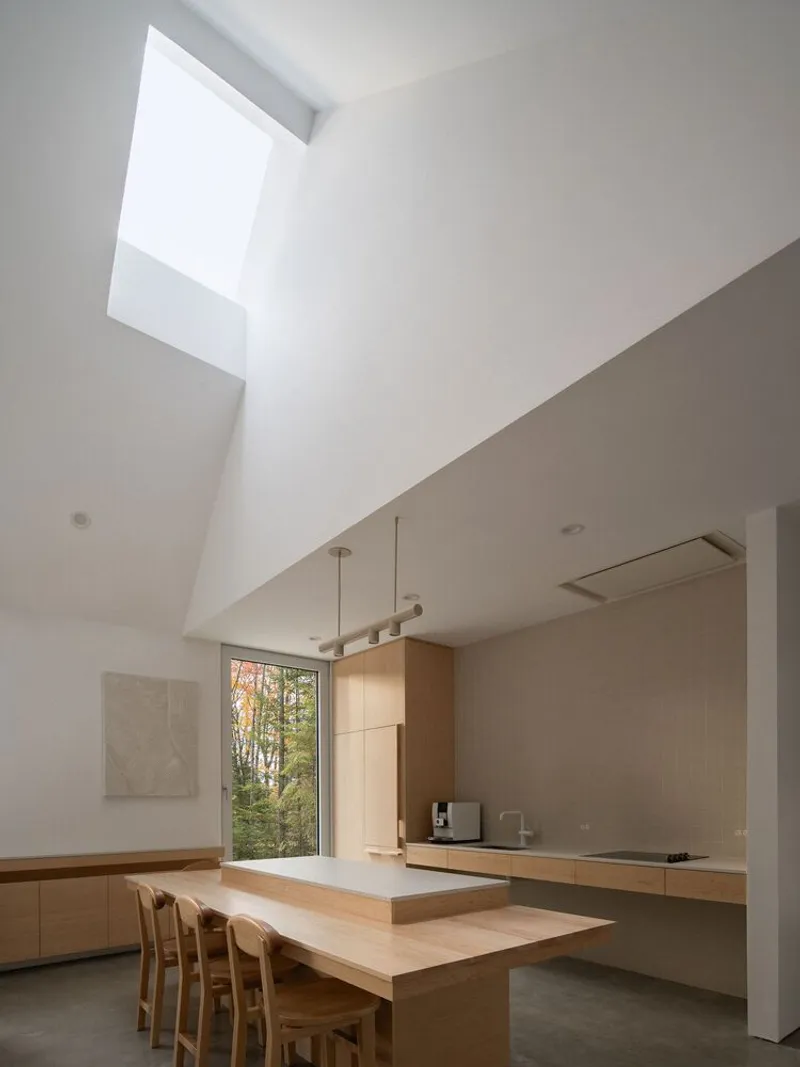 Kitchen: double-height ceiling with square skylight, oak island, bar stools, pendant light, autumn trees through glass