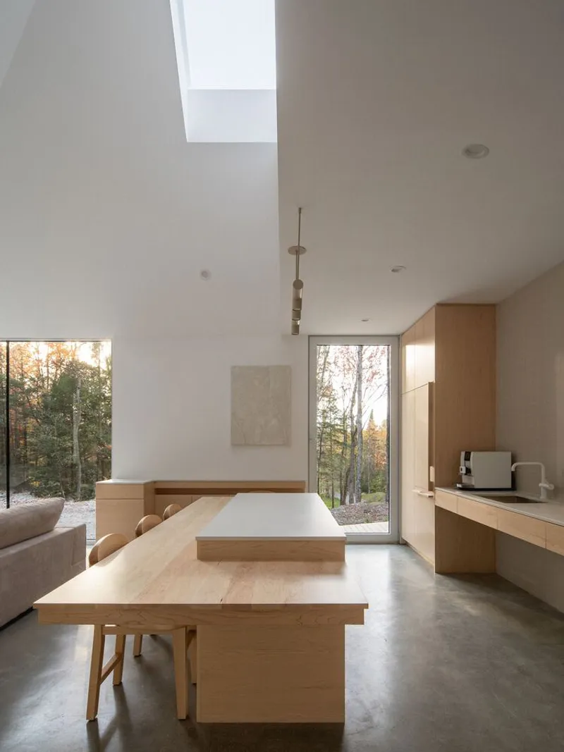 Kitchen from dining: oak island and cabinets, sofa edge visible, skylight washing light down the white walls