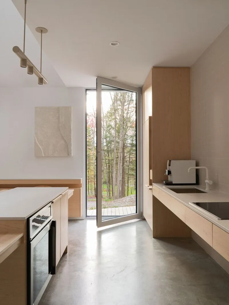 Kitchen corridor: oak cabinets, built-in oven, narrow floor-to-ceiling window framing autumn trees