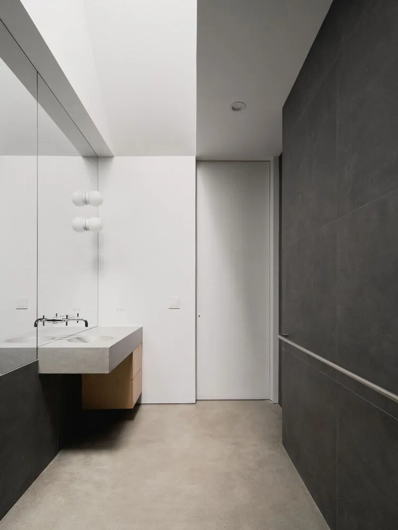 Bathroom: dark grey stone walls, white wall-mounted basin, oak vanity, angular ceiling line