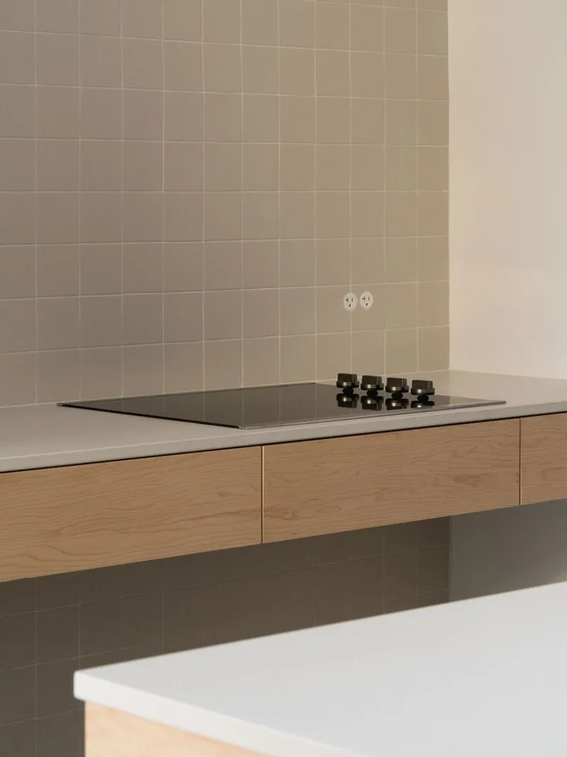 Kitchen detail: beige square tile backsplash, induction hob on oak counter, espresso cups