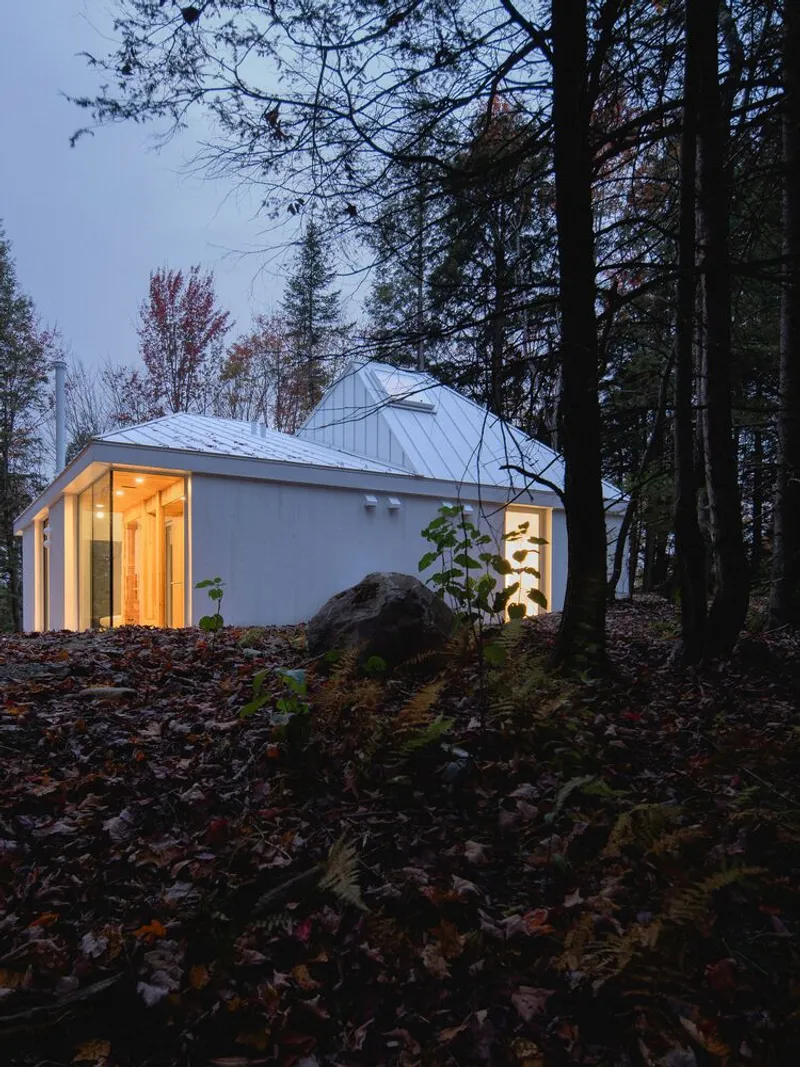 Night through forest: white house lit from within, boulder in foreground, autumn canopy above