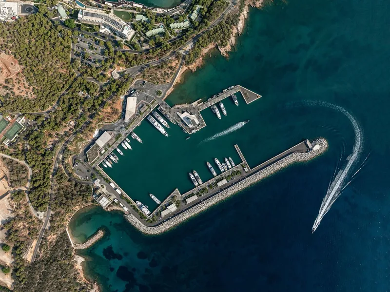Aerial view of the curved stone breakwater enclosing the marina basin with docked yachts