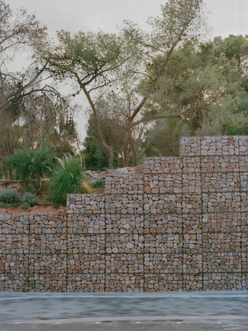 Stepped gabion wall retaining system with native trees visible above the stone-filled wire cages