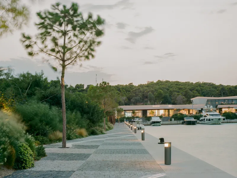 Paved waterfront promenade with patterned stone paving and bollard lights at dusk beside a marina