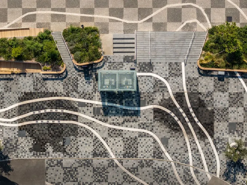 Overhead view of checkerboard stone paving with curving white pathways and glass skylight pavilion