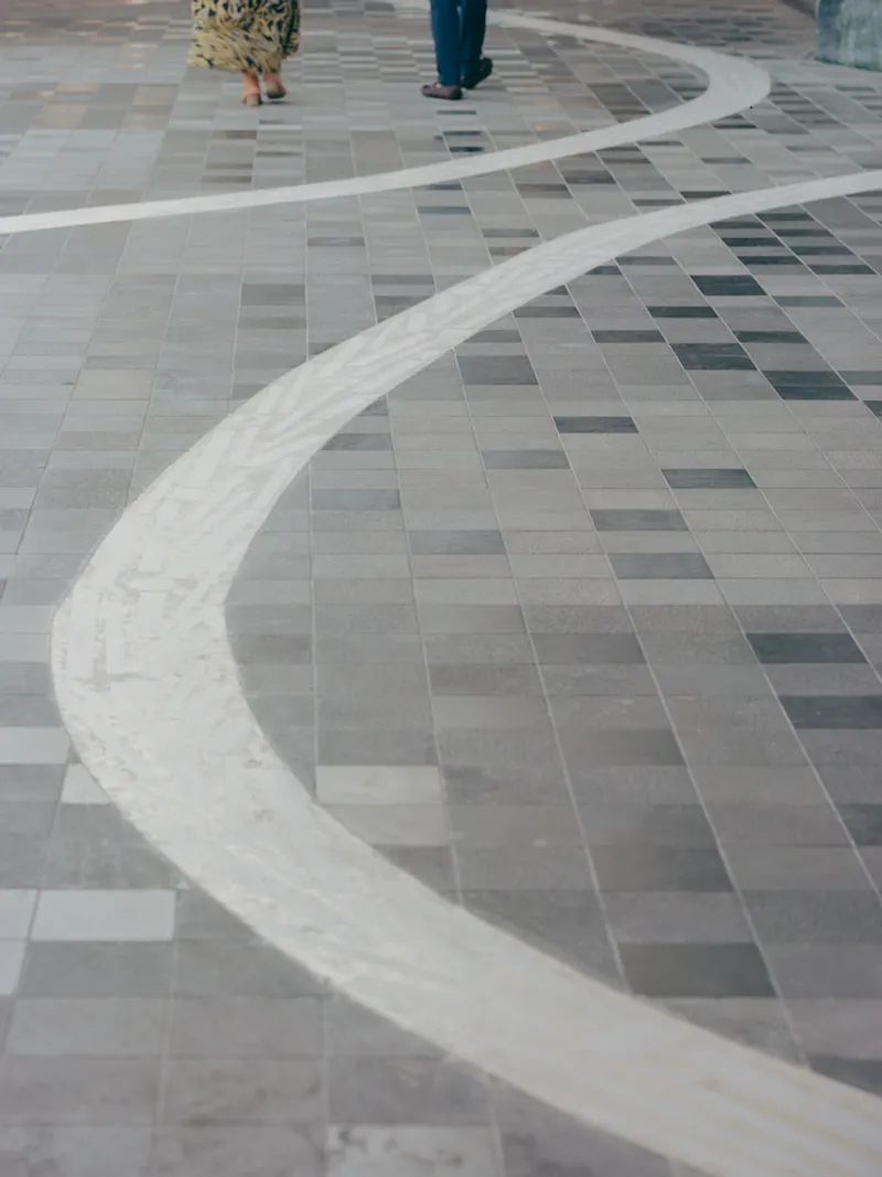 Ground-level view of curved stone border embedded in multi-toned paver pattern with pedestrians walking