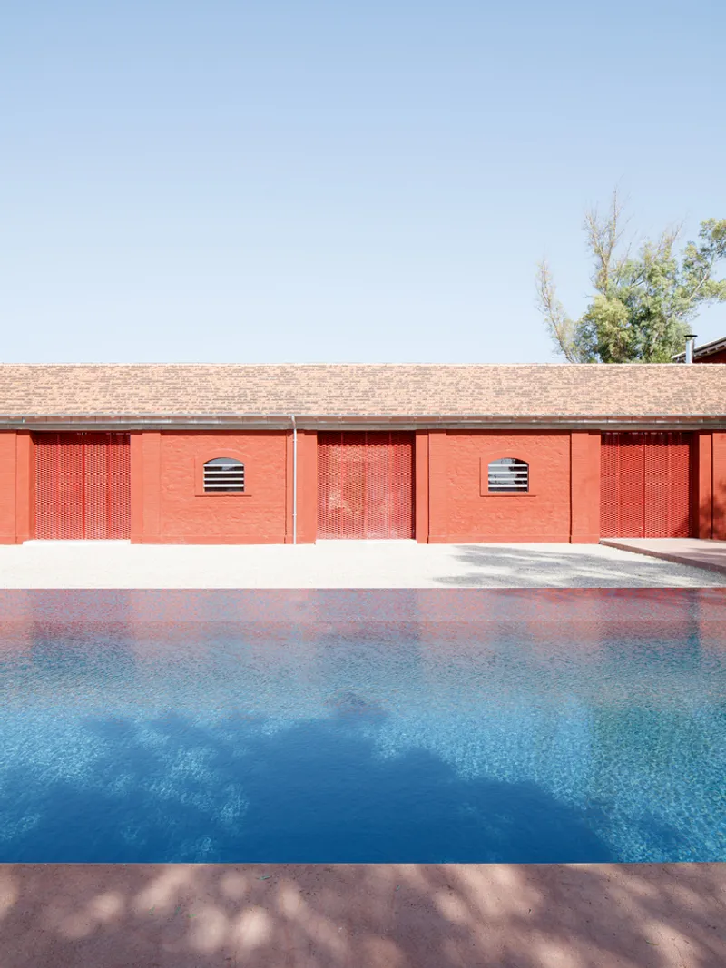 Poolside view of red perforated wall panels with horizontal ventilation slots under clear sky