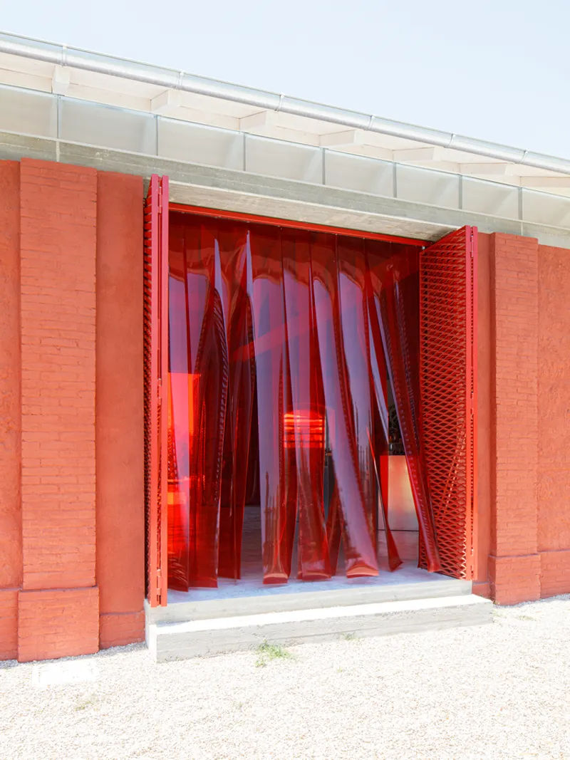 Entry threshold with red translucent strip curtains and textured brick jambs in daylight
