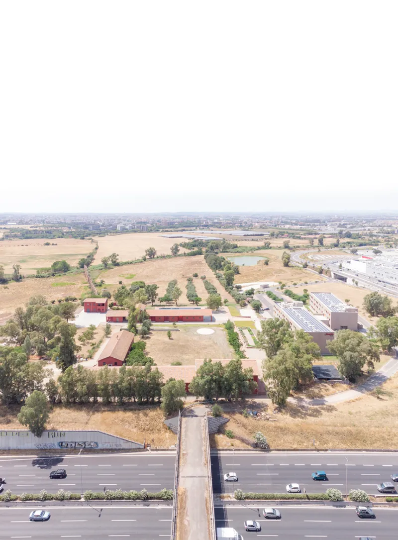 Aerial view of red agricultural buildings arranged in a geometric grid amid fields and trees
