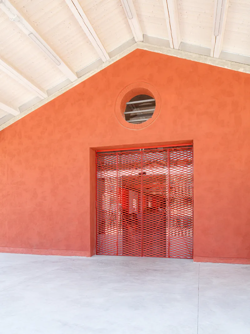 Orange stucco facade with red mesh gate and circular window beneath a white timber ceiling