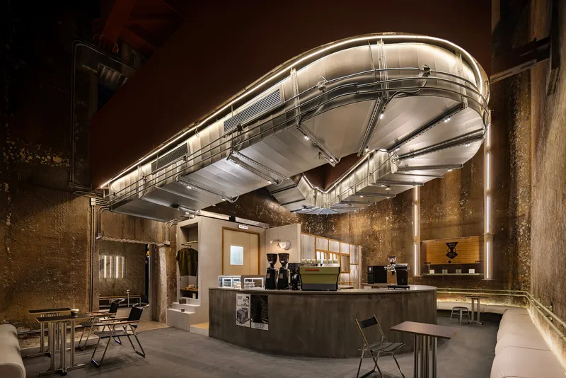 Interior with curved suspended ductwork canopy above a central counter under textured masonry walls at night