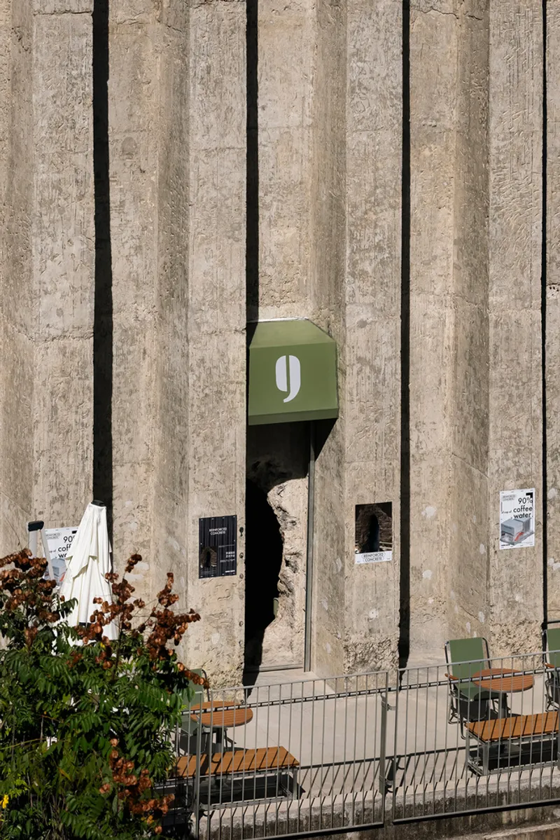 Exterior wall with vertical concrete ribs and recessed openings beside outdoor seating with autumn foliage