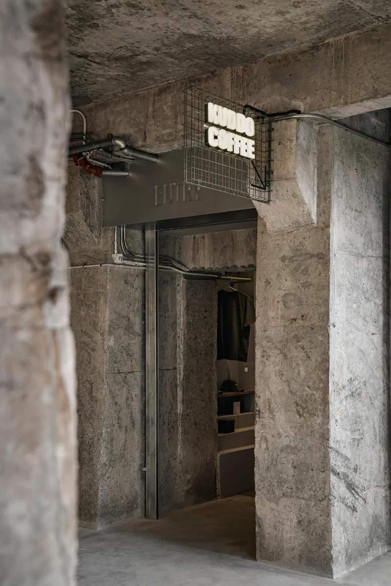 Doorway with exposed conduit and illuminated signage set within board-formed concrete walls and columns