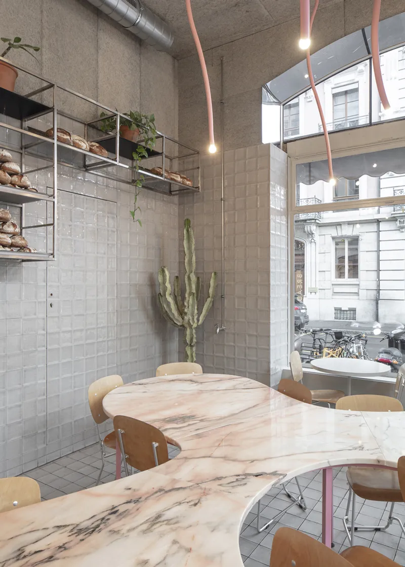 Marble table and ceiling mirror: arched mirror reflecting the street, grey tiles, copper tube lights, cactus, plywood chairs