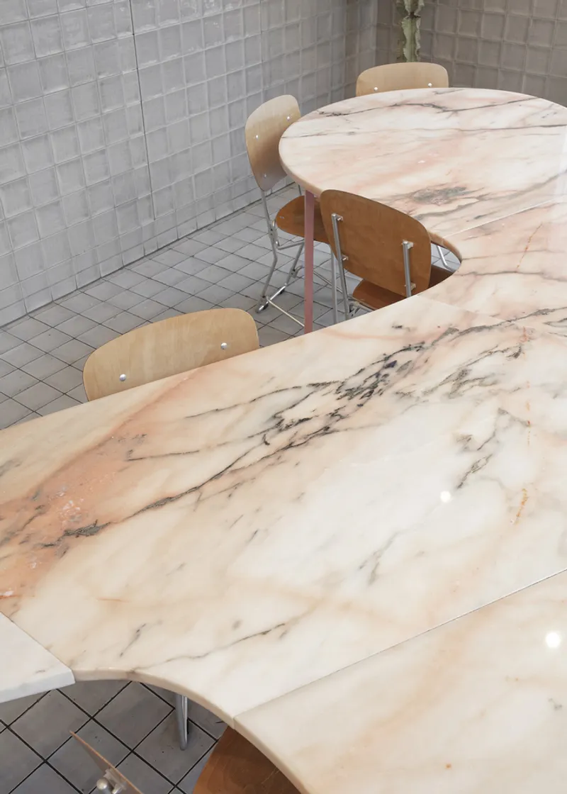 Detail: marble table surface with pink and cream veining, grey tile floor and wall meeting at the base