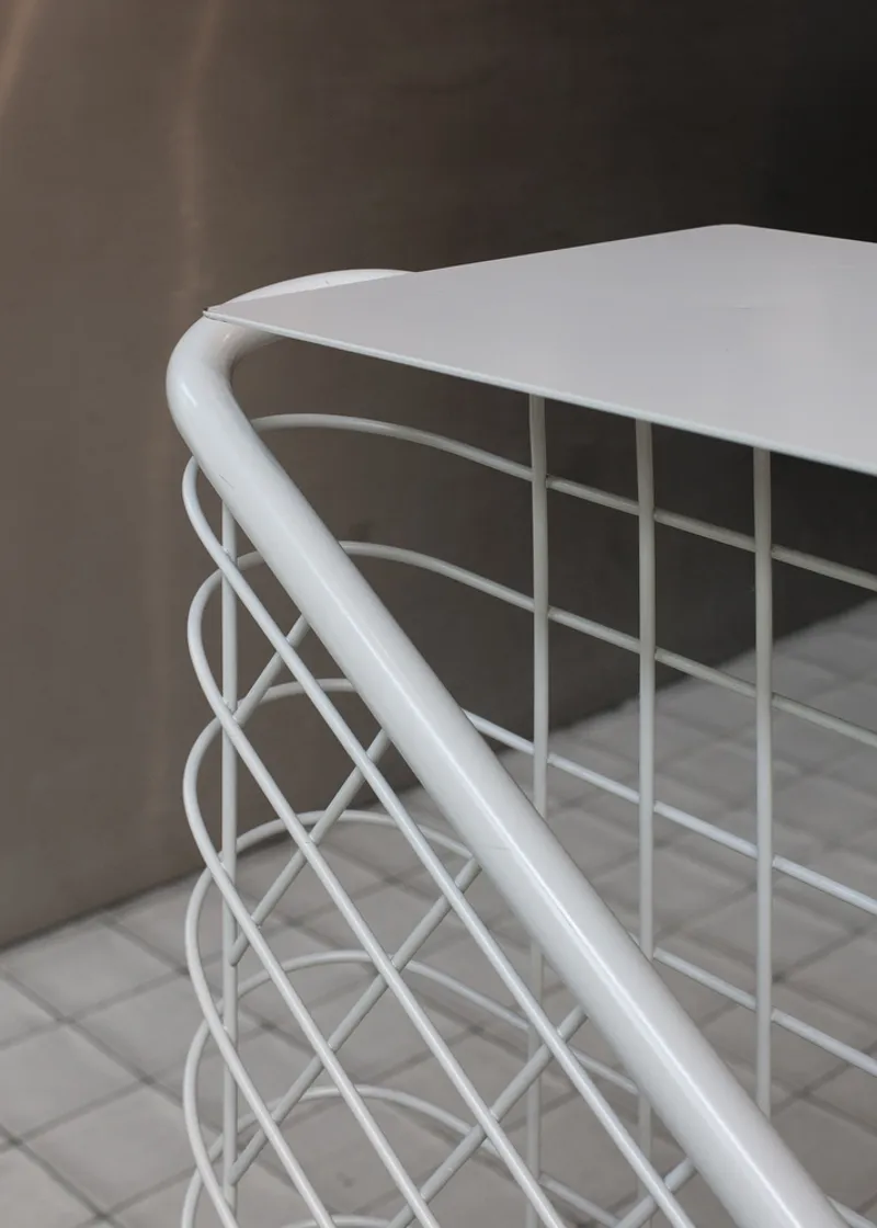 Detail: white wire mesh counter corner with rounded tubular steel frame, grey tile floor