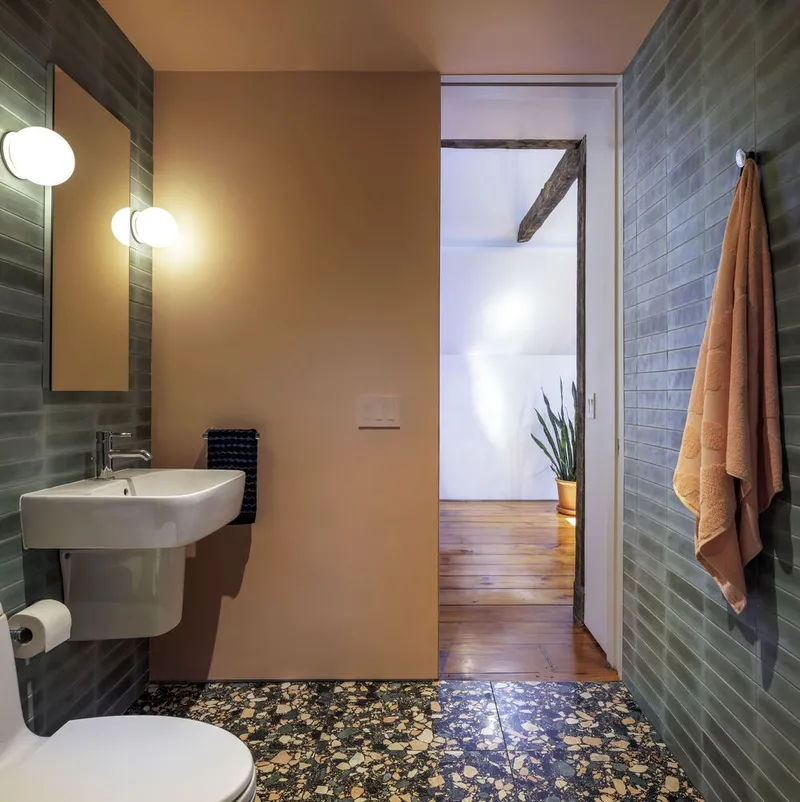 Powder room with grey subway tile walls, wall-hung sink, terrazzo floor, and doorway to timber-floored hallway