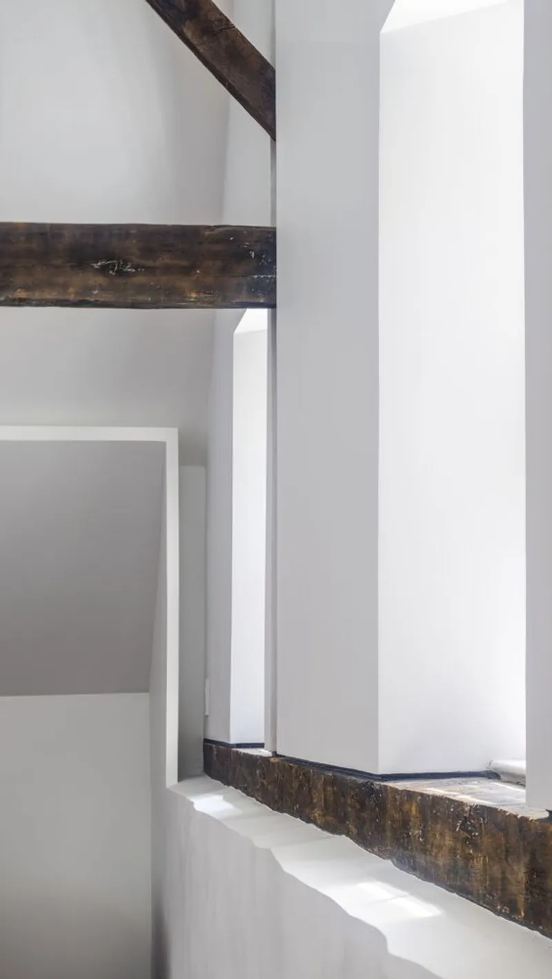 Close-up detail of white wall intersecting with exposed timber beam in bright natural light